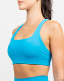 Close-up back detail of the Azure Blue Nexletica Synergy Sports Bra showing the strappy back design and NEXLETICA logo band