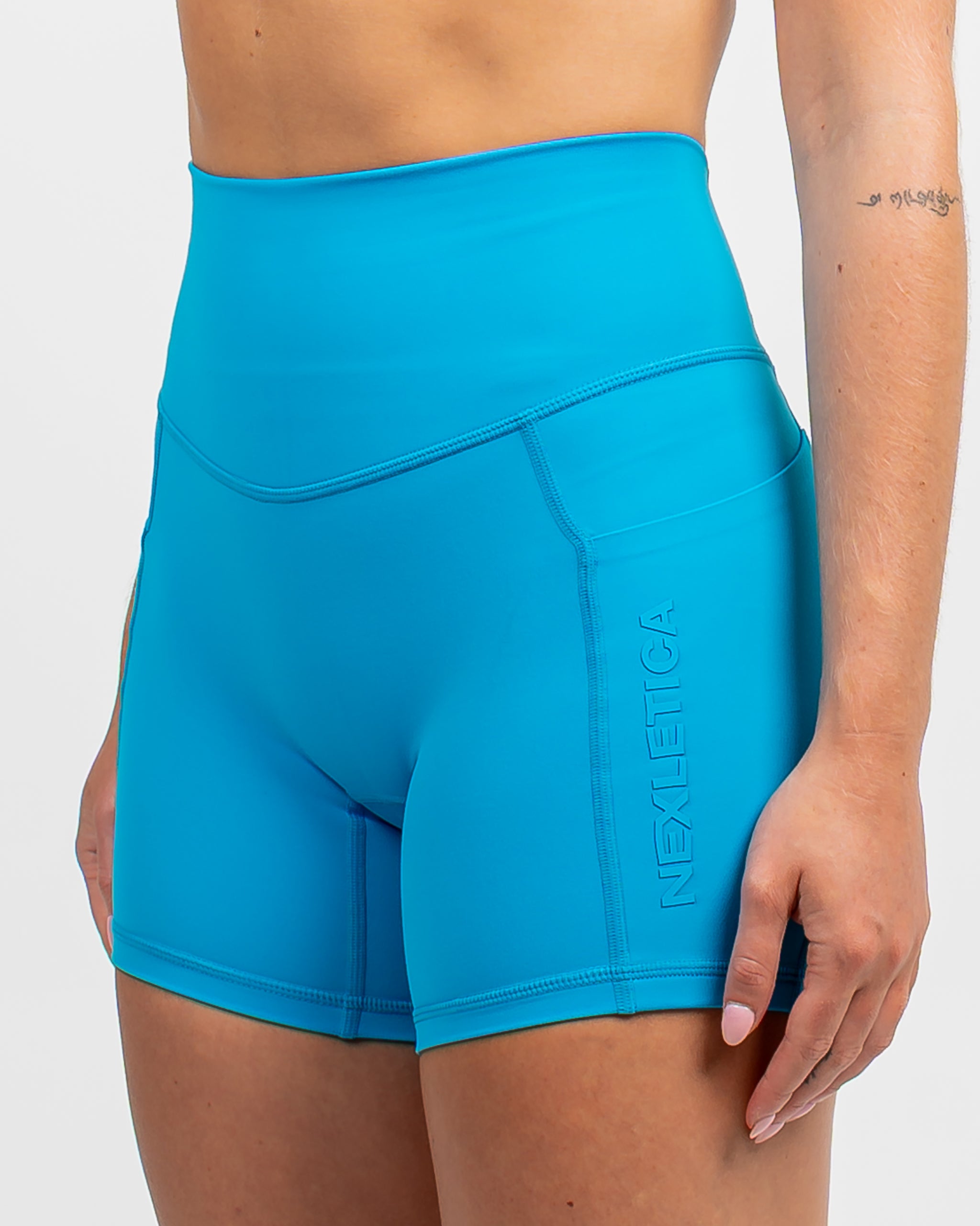 Close-up side detail of the Azure Blue Nexletica Synergy Rise Shorts showing the dual side pockets and tonal NEXLETICA branding