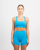 Front view of a woman wearing the Azure Blue Nexletica Synergy Sports Bra with matching shorts, showing the square neckline and thick supportive straps