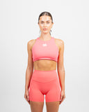 Front view of woman wearing coral Nexletica Impulse High Neck Sports Bra for women’s hybrid training