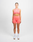 Full body view of model in coral Impulse High Neck Sports Bra styled with matching high waist shorts