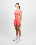 Three quarter side view of model wearing coral Impulse High Waist Shorts and High Neck Sports Bra for women’s hybrid training