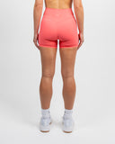 Back view of coral Nexletica Impulse High Waist Shorts and matching high neck sports bra set on model
